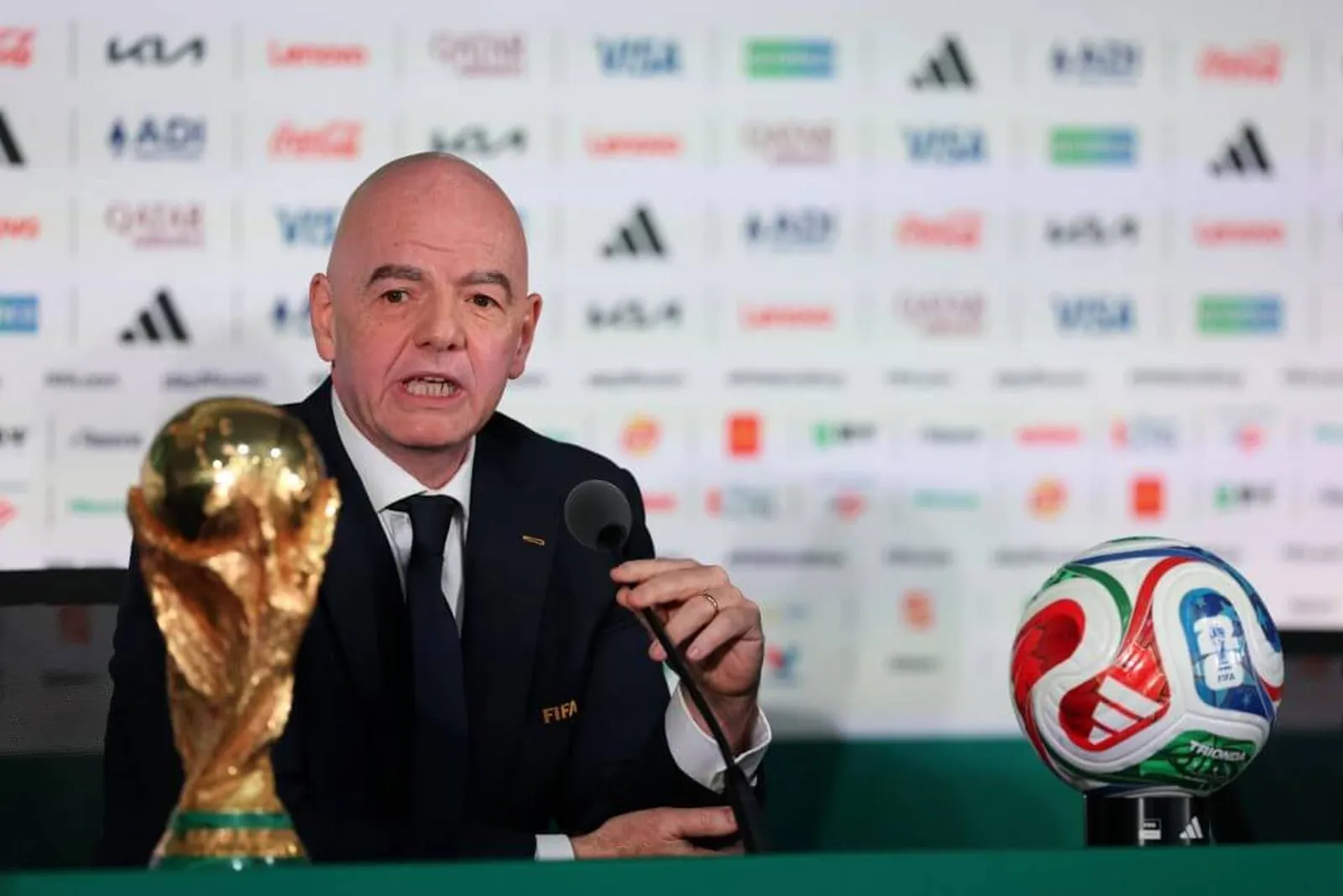 Infantino sitting in a press conference behind the World Cup trophy
